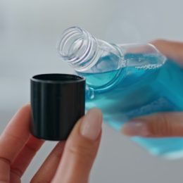 Woman hands pouring mouthwash in cap indoors close up. Unknown lady holding blue antibacterial liquid at bathroom. Unrecognizable girl using refreshing dental rinse. Morning care in bath room concept