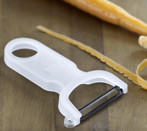 A white peeler on a wood background next to a carrot