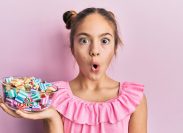 girl holding jar full of sugar candies against a pink background