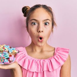 girl holding jar full of sugar candies against a pink background