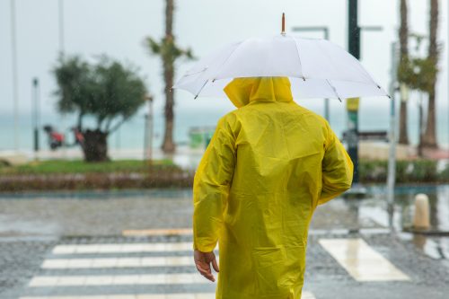 A man standing in a crosswalk in a rainstorm while wearing a raincoat and using an umbrella