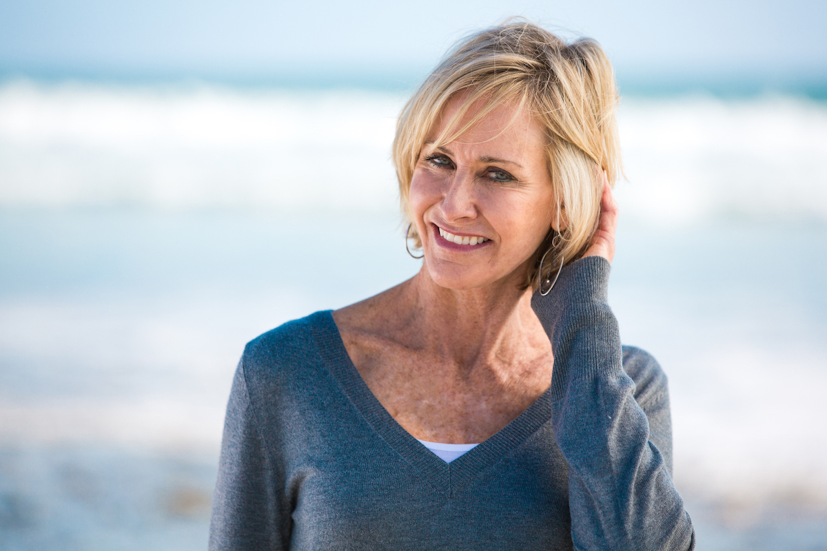 A mature woman wearing a v-neck blue sweater on the beach