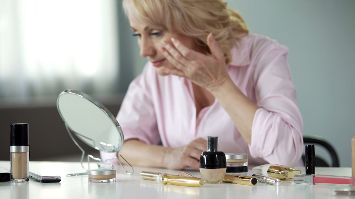 woman in pink shirt applying makeup with makeup mirror