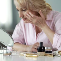 woman in pink shirt applying makeup with makeup mirror