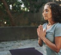 Mature woman meditating with her eyes closed on an exercise mat during a yoga session outside in a courtyard