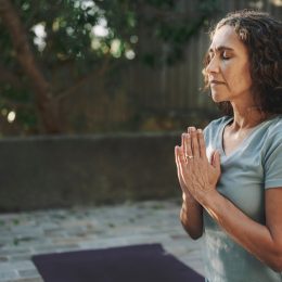 Mature woman meditating with her eyes closed on an exercise mat during a yoga session outside in a courtyard