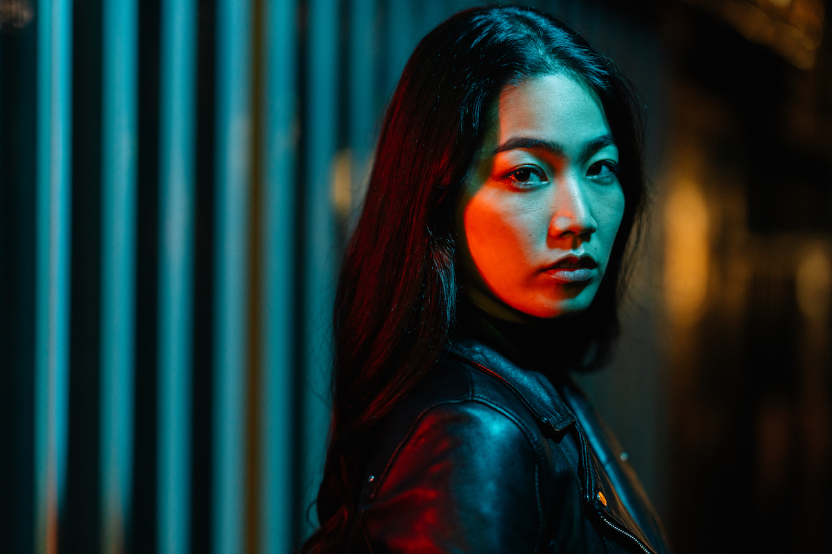 A portrait of a young mysterious-looking woman lit by neon colored light in the city at night.