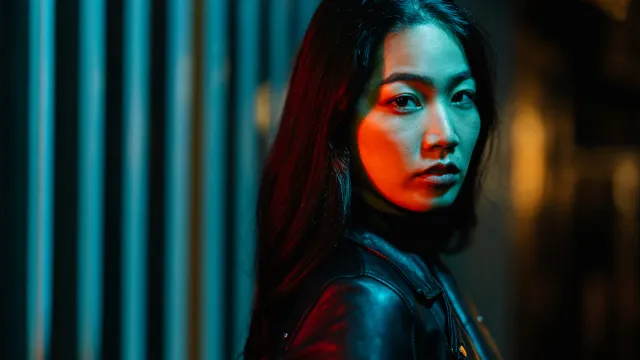 A portrait of a young mysterious-looking woman lit by neon colored light in the city at night.