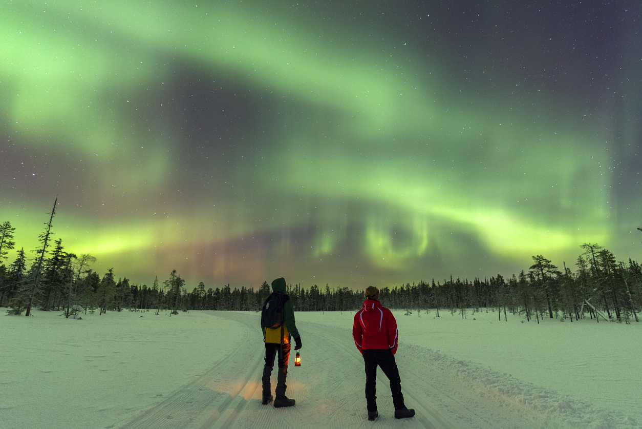 Two people watching the Northern Lights outside in the snow