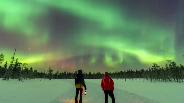 Two people watching the Northern Lights outside in the snow