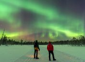 Two people watching the Northern Lights outside in the snow