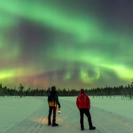 Two people watching the Northern Lights outside in the snow