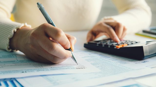 A close up of a person filing out a 1044 tax form while using a calculator