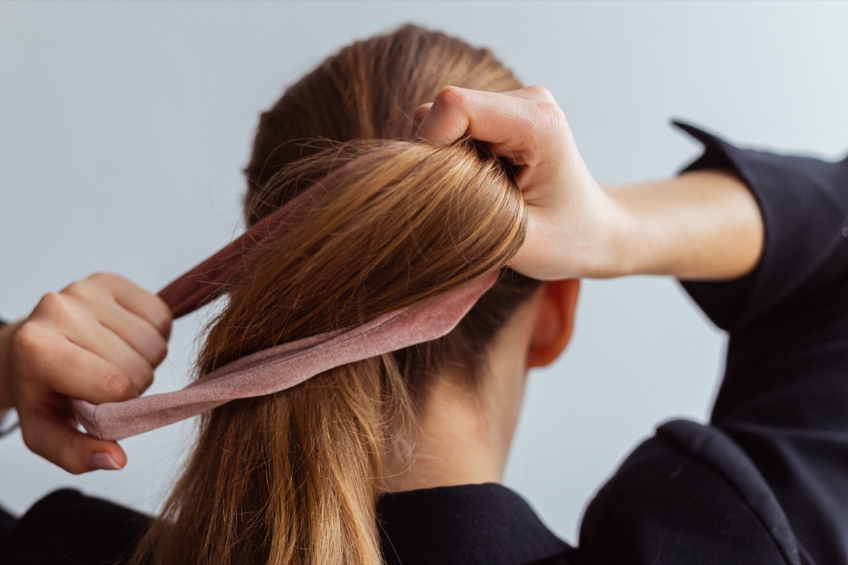 Young woman doing a ponytail with velvet hair tie, scrunchie, view from the back