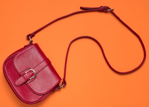 Red leather bag on a long strap on an orange background. 