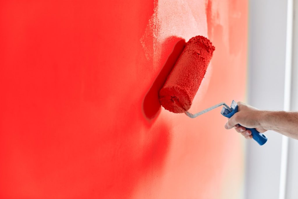 Male hand painting wall red with paint roller
