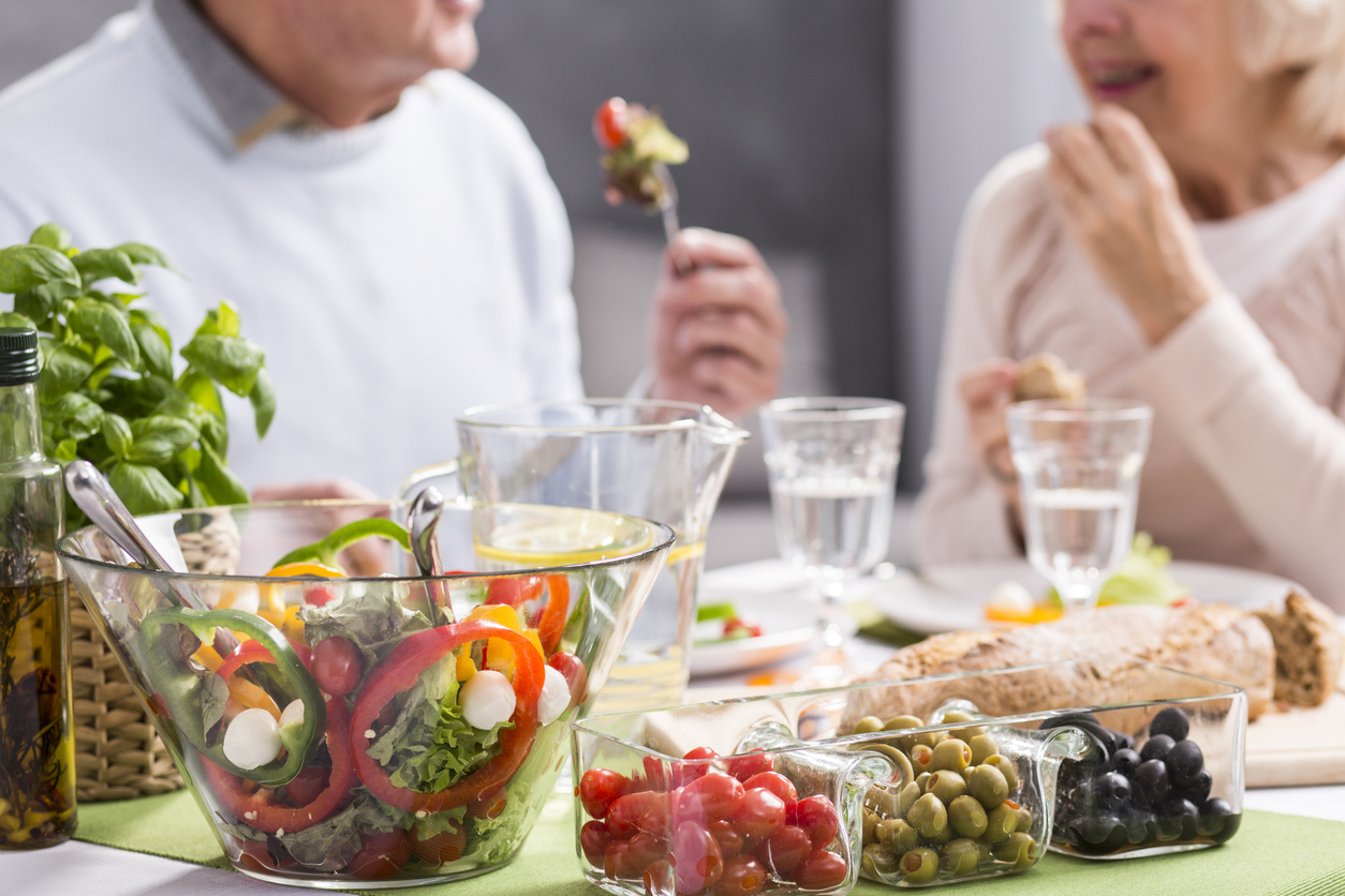A closeup of salad and healthy food while a senior couple eat in the distance