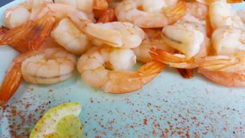Boiled peeled shrimp on a blue plate close-up. Shrimp with lemon and pepper.