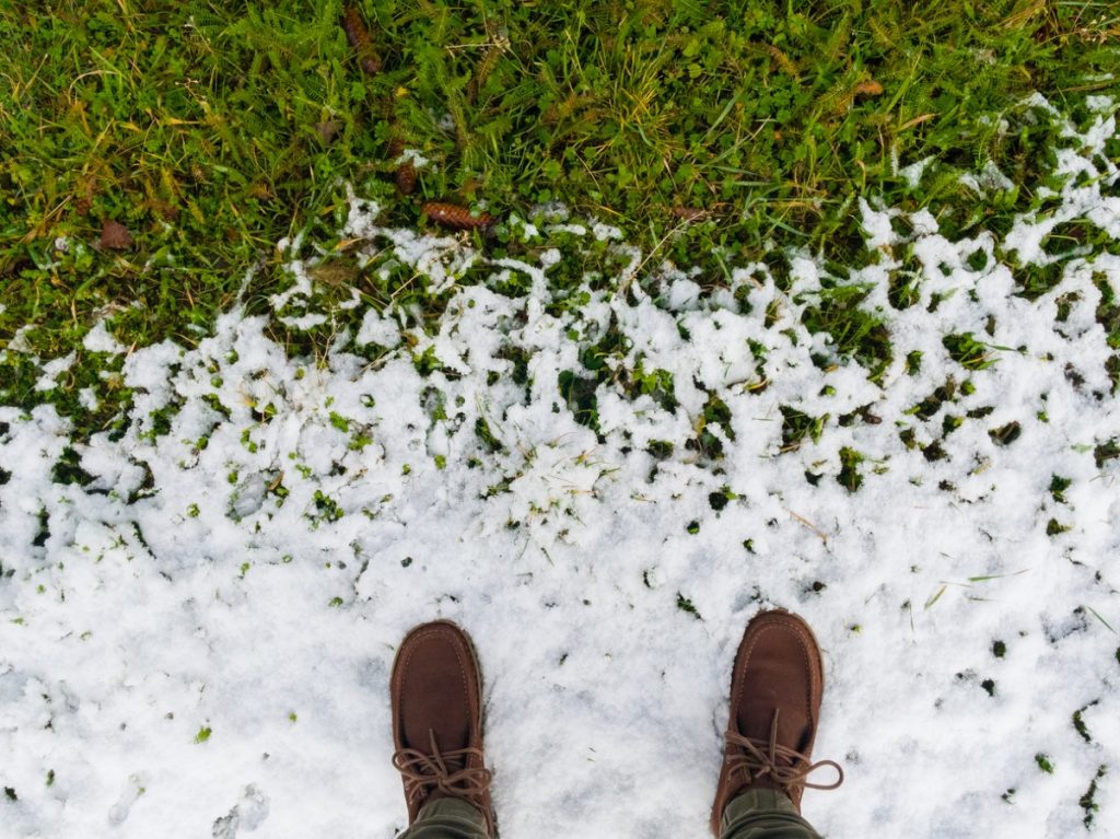 Man in brown boots standing on melting snow on green grass. Conceptual photograph of the movement toward spring. Conceptual image about improving life. View from above.