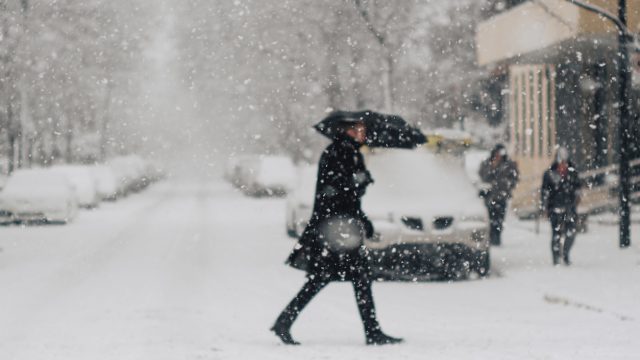 A person crossing the street during a snowstorm while using an umbrella