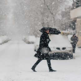 A person crossing the street during a snowstorm while using an umbrella