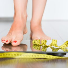 A person stepping on to a scale with a measuring tape in front of her feet