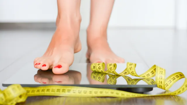 A person stepping on to a scale with a measuring tape in front of her feet