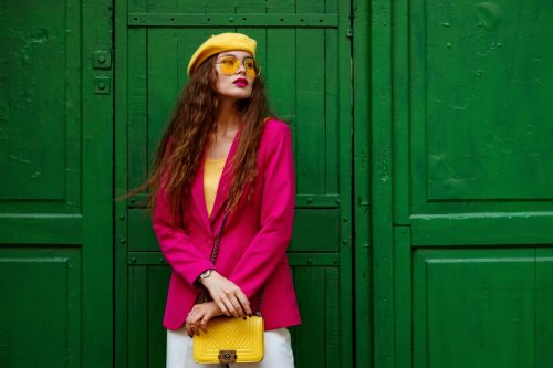 Fashionable confident woman wearing trendy outfit with yellow sunglasses, beret, shoulder bag, pink fuchsia color blazer, posing near green door. Copy, empty space for text