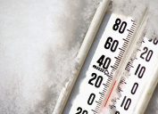 A close up of a thermometer resting in snow reading a low temperature