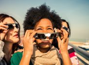 Three happy female friends looking at a solar eclipse, as one woman removes her eclipse glasses