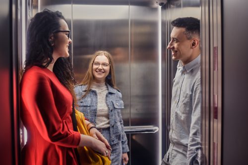 Two young women and a young man talking in an elevator