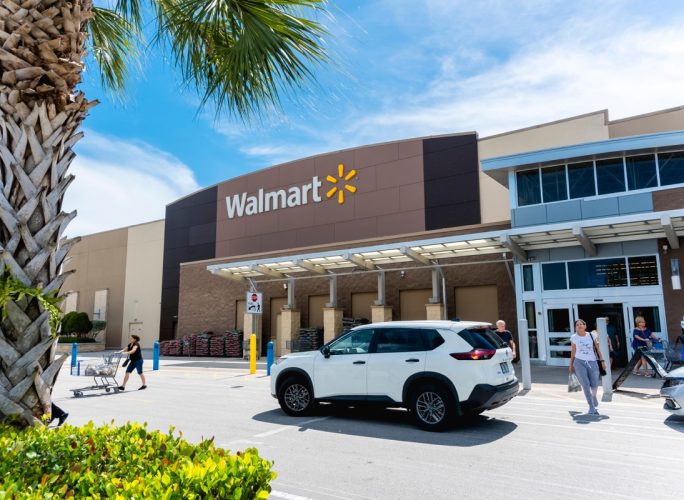 the outside of a Walmart store with customers walking out and a palm tree