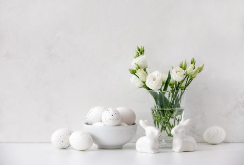 Display of white Easter eggs, white bunny figurines, and white flowers against a white background
