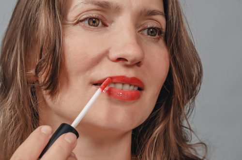 Woman paints her lips with coral-colored lip gloss, close-up.