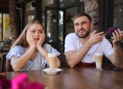 Young woman having boring date with talkative guy in outdoor cafe