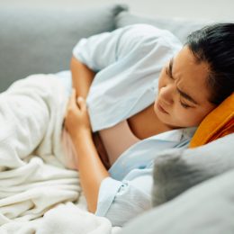 A young woman lying on the couch while holding her stomach with food poisoning symptoms or a stomach ache