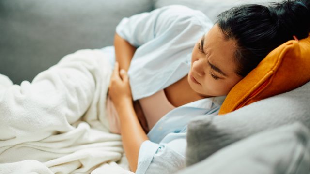 A young woman lying on the couch while holding her stomach with food poisoning symptoms or a stomach ache