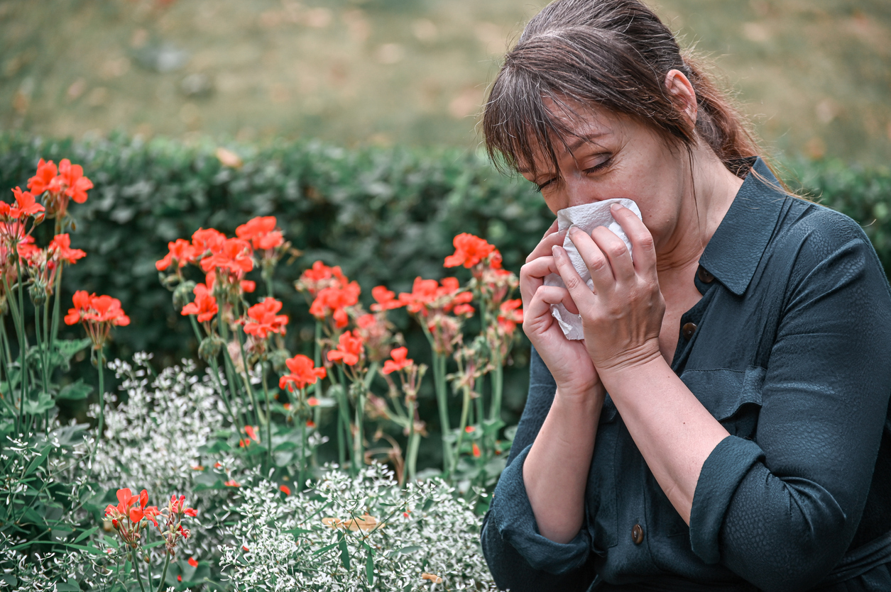 A woman sneezing while standing next to flowers in a garden