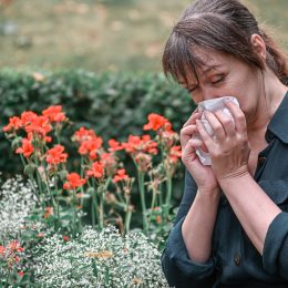 A woman sneezing while standing next to flowers in a garden