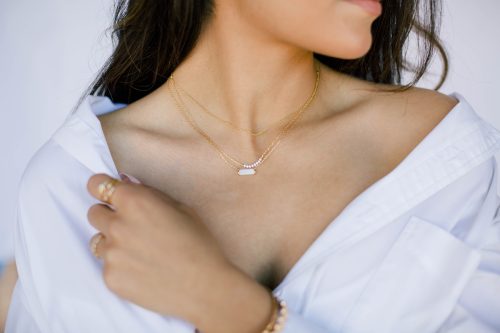Close up of a woman's chest; she is wearing a white blouse and dainty gold necklaces