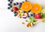 Multivitamins and supplements with fresh and healthy fruits on white wooden background.