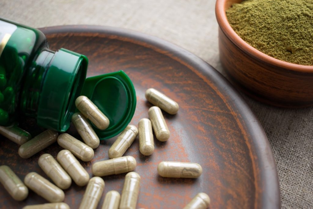 Close up Green capsules, bottle and powder on a clay brown plate on a burlap background