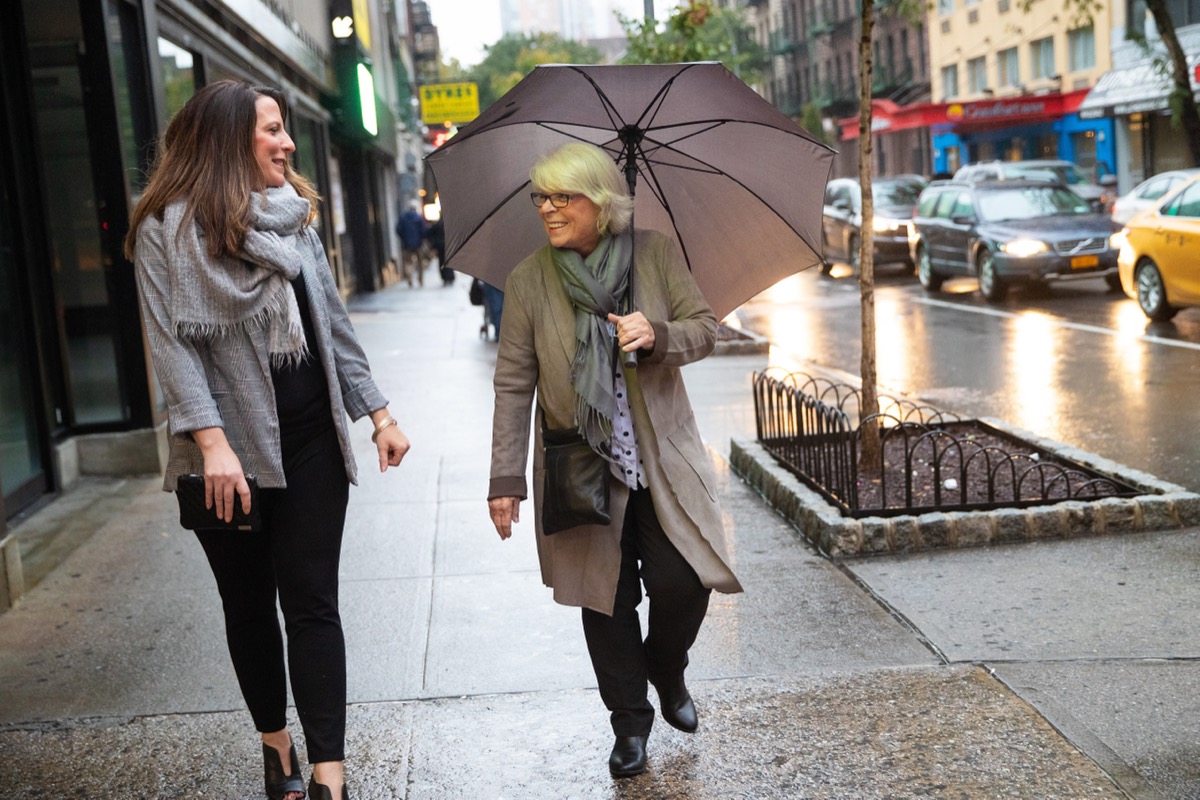 Two women walking together under umbrella on rainy day in city