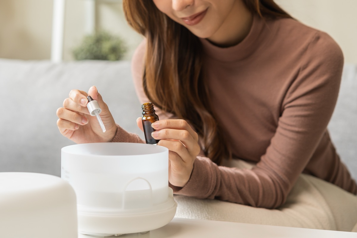 Close up of a young woman adding oil to her aromatherapy diffuser while sitting on her couch