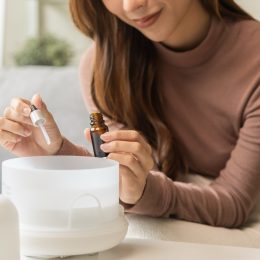 Close up of a young woman adding oil to her aromatherapy diffuser while sitting on her couch