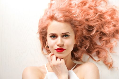 Trendy hairstyle ideas. Young woman with dyed apricot hair on white wooden background