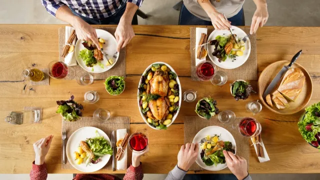 Top view of dining table with salad and roasted chicken with potatoes. High angle view of happy young friends having lunch at home. Men and women eating lunch together.