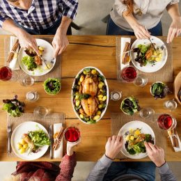Top view of dining table with salad and roasted chicken with potatoes. High angle view of happy young friends having lunch at home. Men and women eating lunch together.