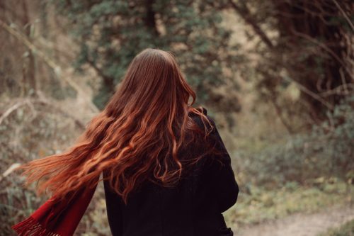 Back portrait of redhead girl with beautiful long and wavy hair shaking her head