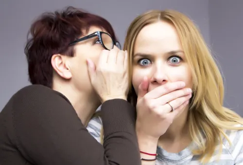 woman whispering in shocked woman's ear